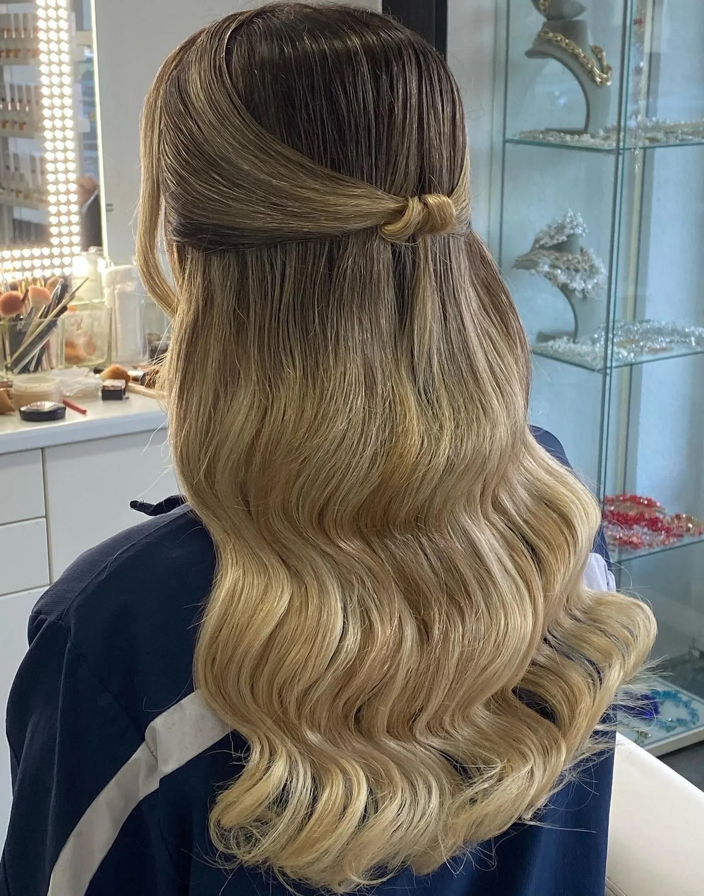 Blond ombre haar in zachte golven, half opgestoken met een knoopje, van achteren