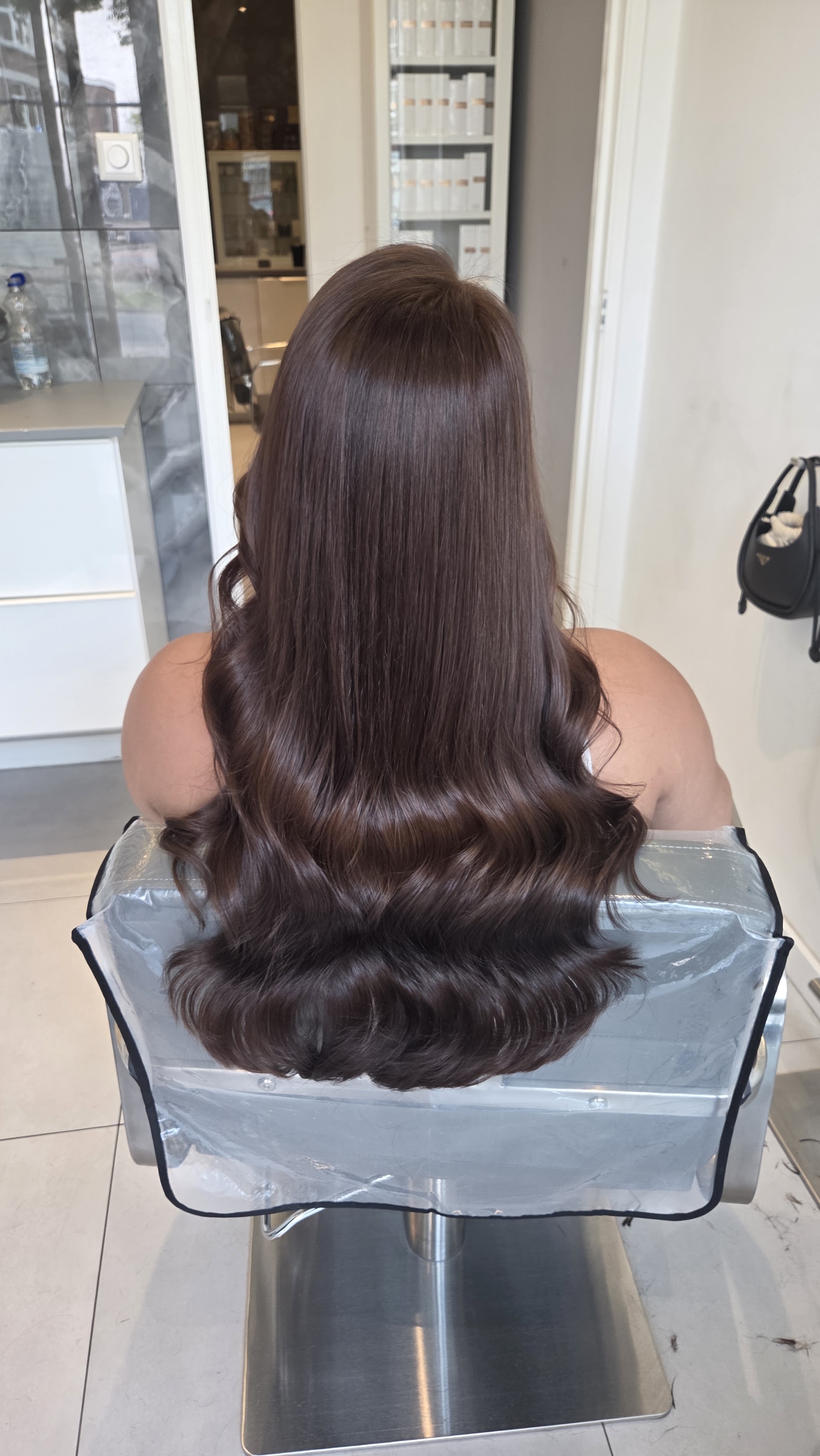 Lang donkerbruin haar met golven in de punten, van achteren in de kappersstoel